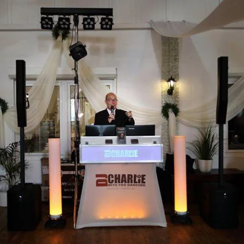 DJ Charlie hinter seinem DJ Pult auf einer Feier mit Mikrofon in der Hand